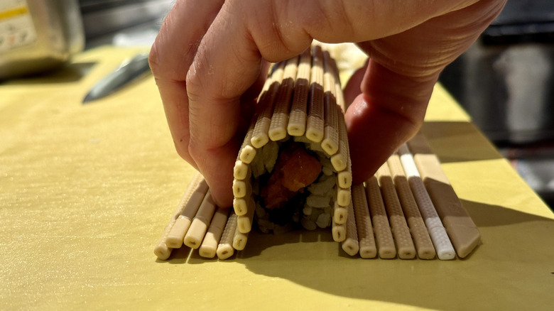 Hands pressing a sushi roll with bamboo mat