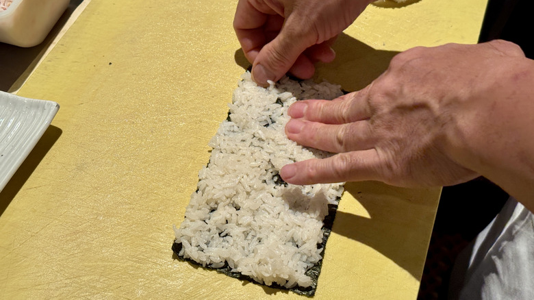 Chef's hands spreading rice over a piece of nori
