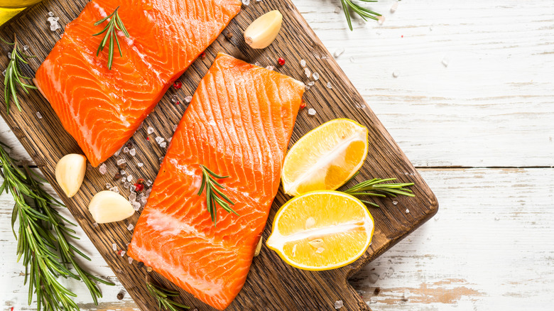 Two fillets of uncooked salmon arranged on a wooden cutting board