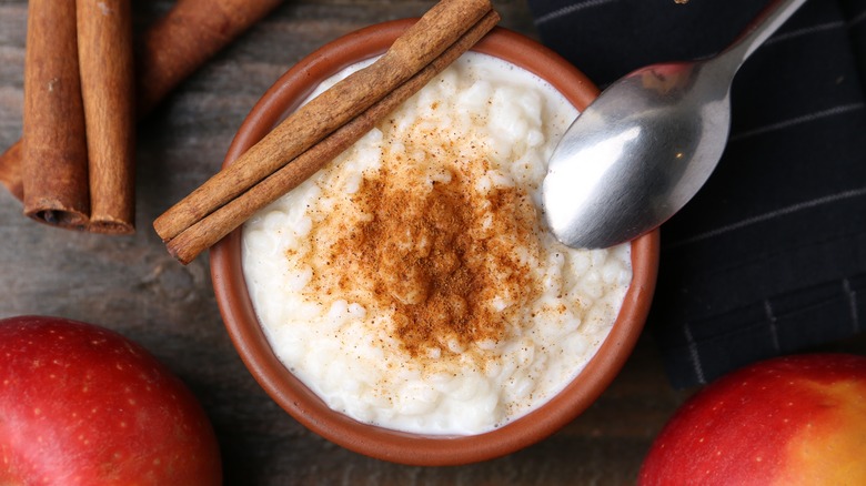 Rice pudding with cinnamon sticks and apples on wooden table