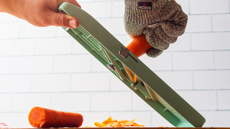 A person wearing gloves and cutting a carrot using a mandoline