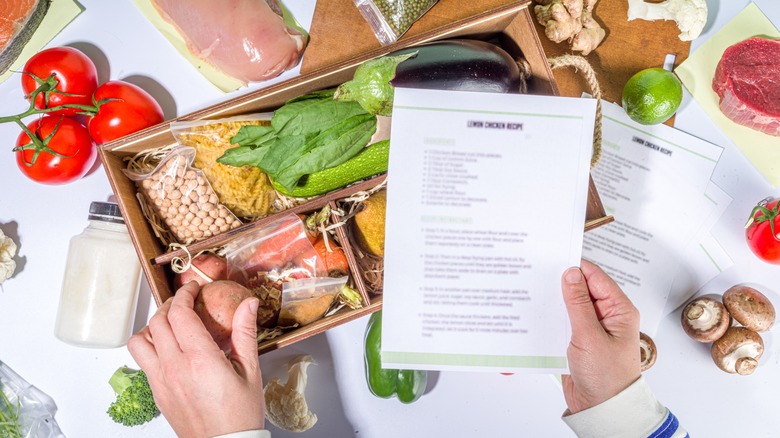 Hands holding a meal kit with ingredients displayed on white counter
