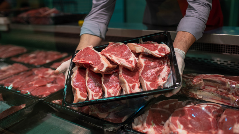 Butcher holding a large platter of cut steaks above a display