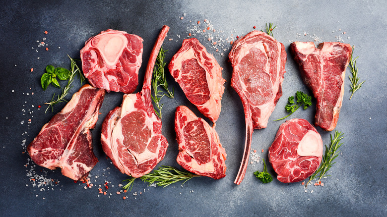 Various cuts of raw steak sitting on a black background surrounded by herbs
