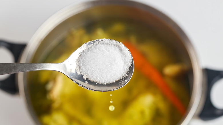 A metal spoon is being used to add salt to a pot of soup