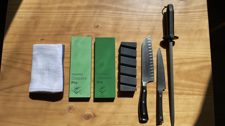 A towel, 400 grit stone, 1000 grit stone, flattening stone, knives, and honing steel on a table