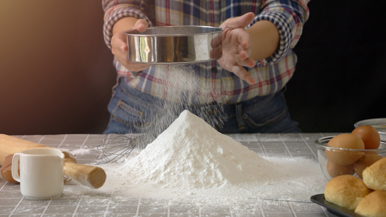 Person using a fine mesh strainer to sift flour