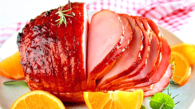 Glazed, pre-sliced ham surrounded by orange slices and fresh herbs