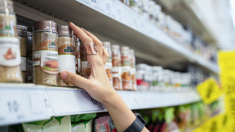 A woman selecting spices from a grocery store shelf