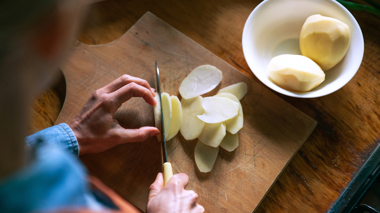 Close-up on a woman cutting potatoes on a chopping board while cooking at home