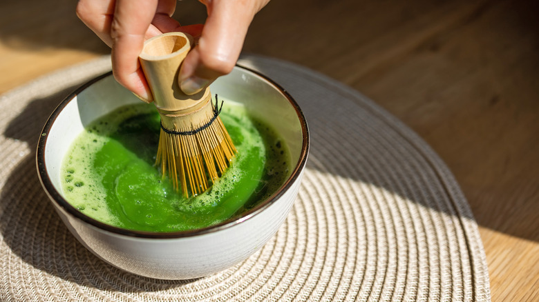 Hand whisking matcha in a white bowl