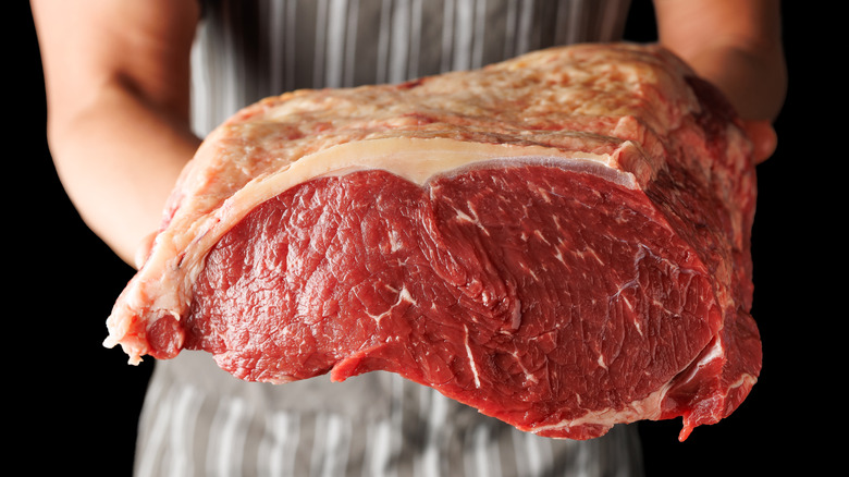 A person in a butcher's apron holding a large sirloin steak.