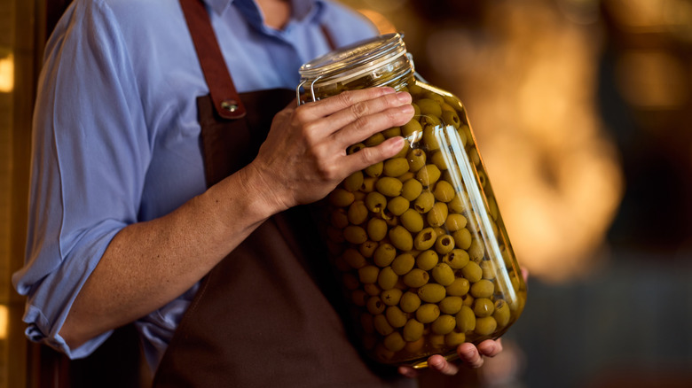 Close-up of hands holding a large jar of olives.