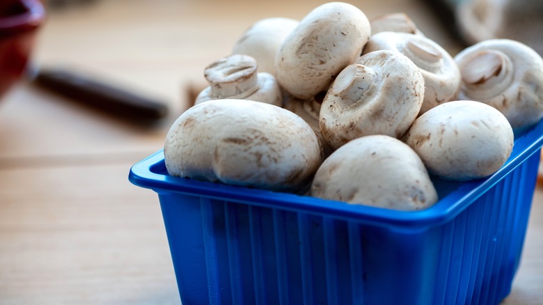 Raw white button mushrooms in plastic container