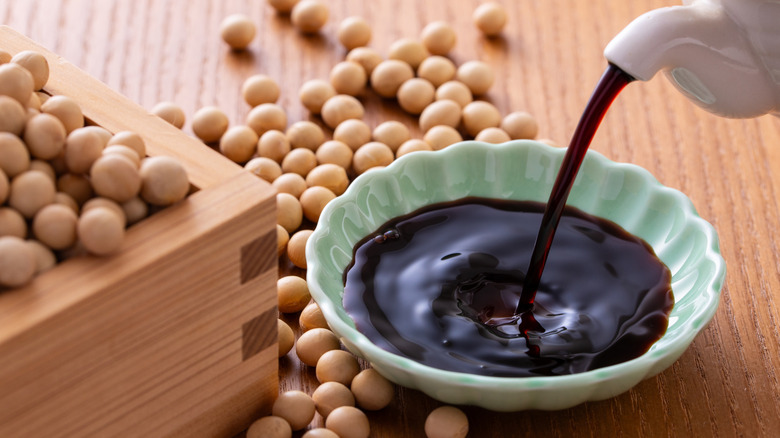 Soy sauce being poured into a small bowl on a table.