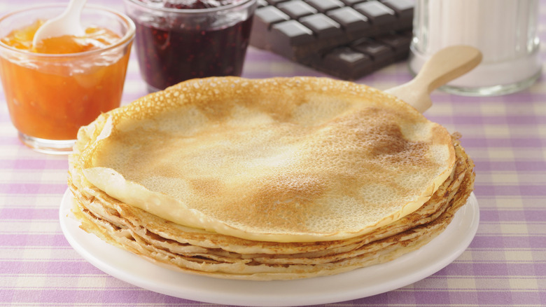 Crepes on white plate next to jars of jam