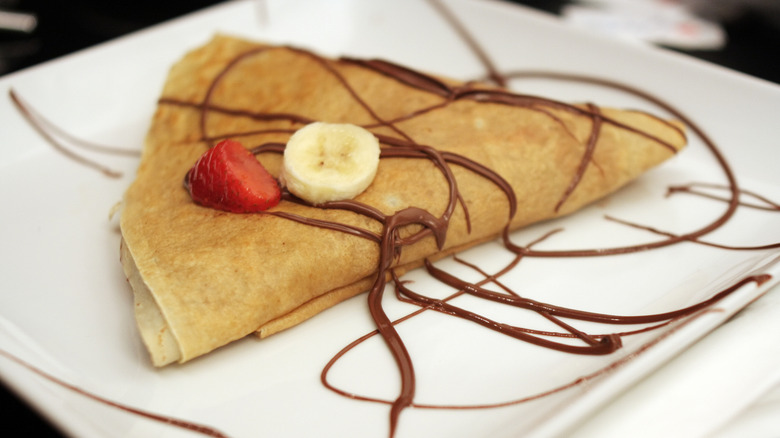 A crepe topped with Nutella, a slice of banana, and a strawberry