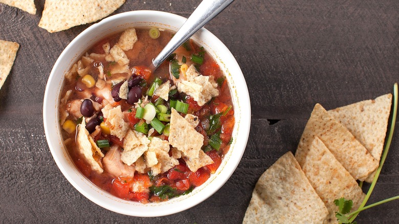 Top-down view of chili with crushed tortilla chips in a white bowl with a metal spoon