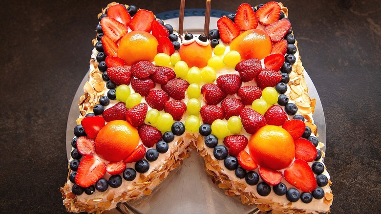 Butterfly-shaped cake covered in mixed fruit and lined with sliced almonds