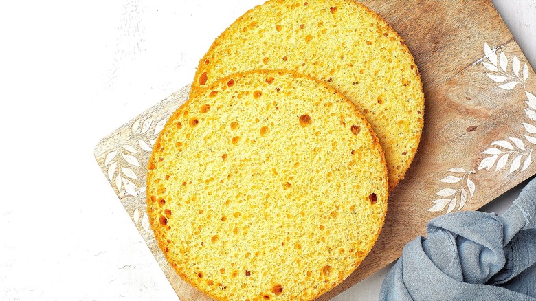 Two round layers of unfrosted vanilla cake on wooden board