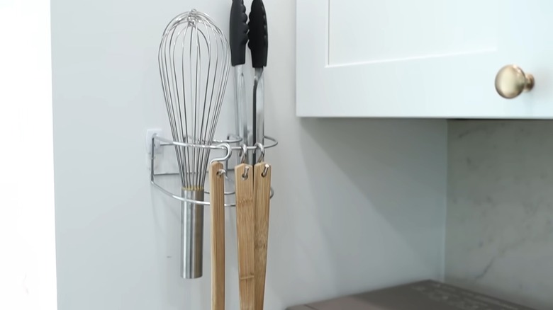 A napkin holder mounted to a wall holding kitchen utensils