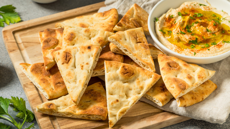 Pita chips stacked on a wooden board next to a bowl of dip.