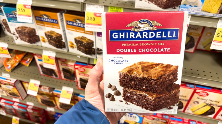 Hand holding Ghirardelli brownie mix in grocery store aisle