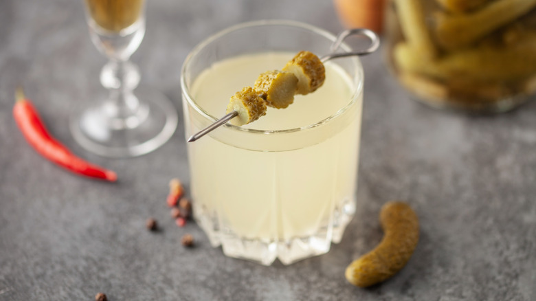 a glass of pickle cocktail with a skewer of pickles