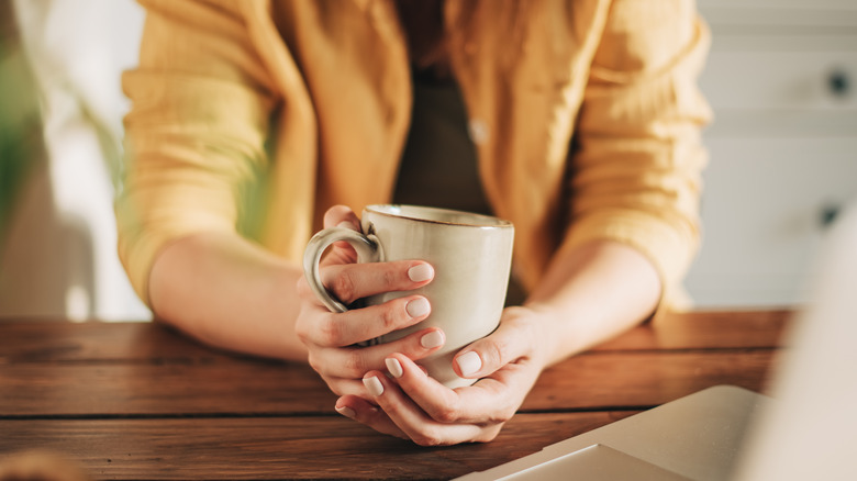 a woman holding a mug on a table with two hands