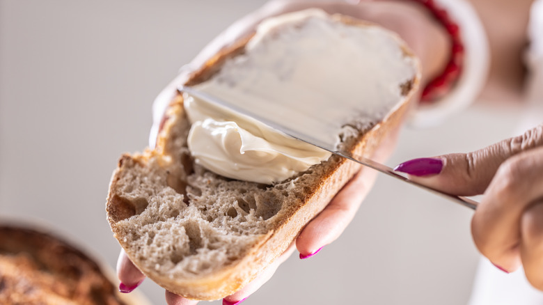 Someone spreading soft butter on a slice of bread with a knife