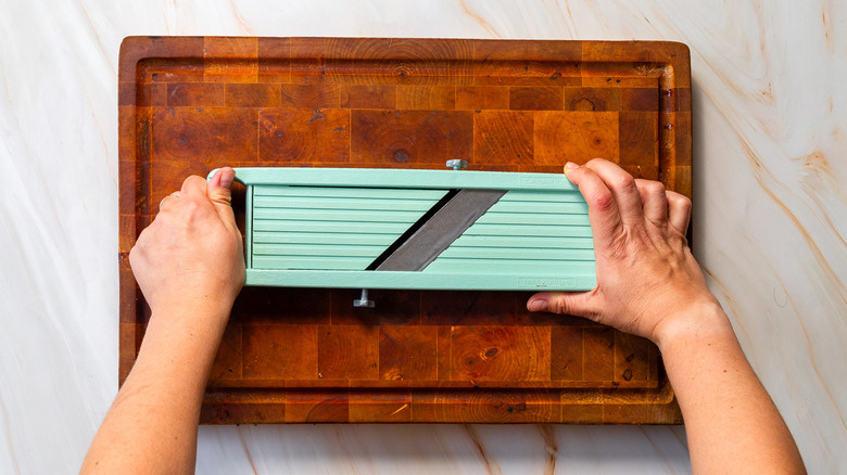Someone holding a mandoline on a wooden cutting board