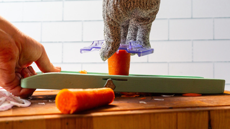 A person cutting a carrot on a mandoline placed on a cutting board