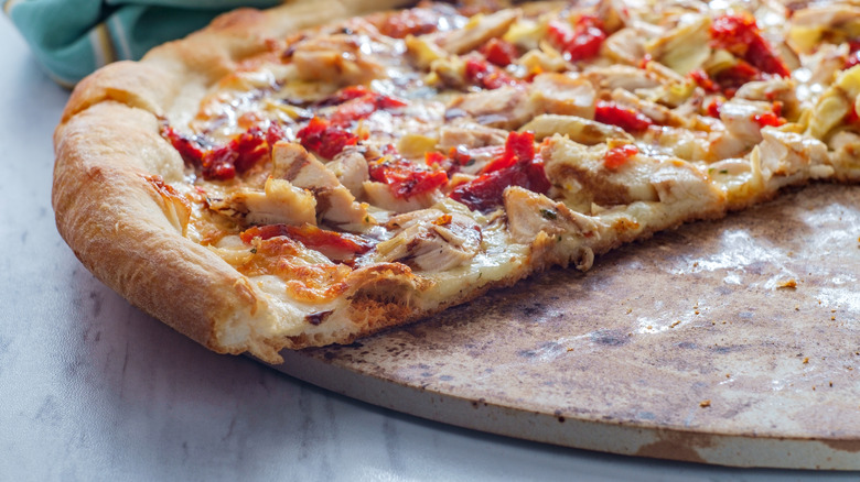 Half a pizza with chicken and peppers sits on a round pizza stone