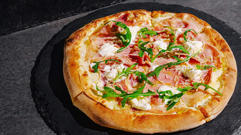 Ham and arugula pizza sitting on a slate pizza stone