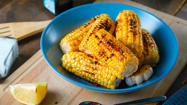 A blue bowl of yellow corn on the cob that's been roasted.