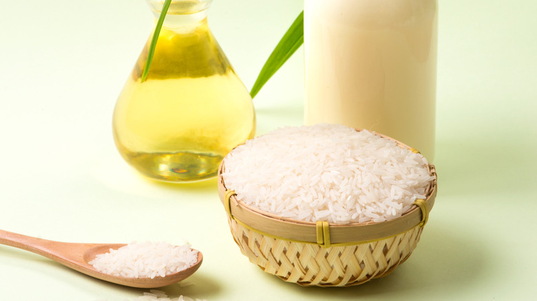Bowl of uncooked rice with oil next to wooden spoon full of uncooked rice