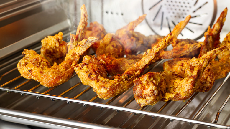 Breaded chicken wings frying on an air fryer oven rack.