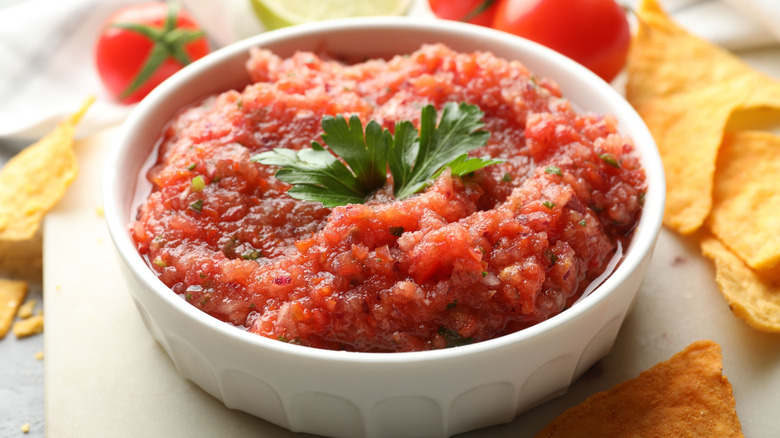 a bowl of fresh tomato salsa sitting in a white bowl surrounded by tortilla chips