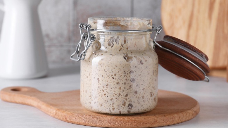 A jar of sourdough starter sits open on a wooden cutting board