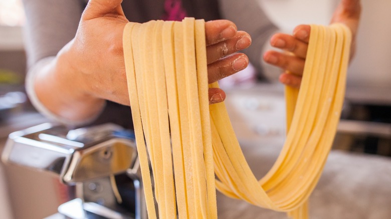 Hands hold strands of fresh pasta straight from the roller