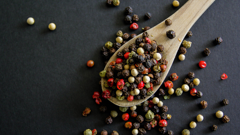 Peppercorns of different colors in wooden spoon