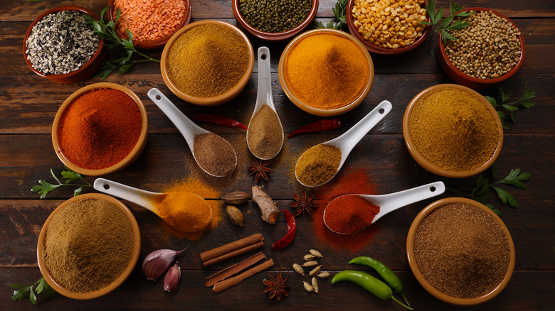 Bowls and measuring spoons of ground spices with bowls of whole spices in background