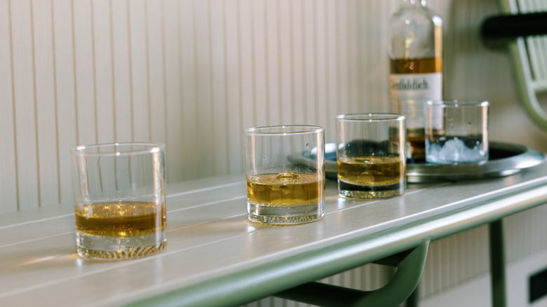 Three whiskey glasses on counter with bottle in the background