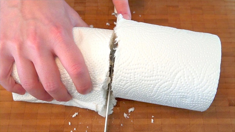 Hand cutting through paper towel roll on cutting board