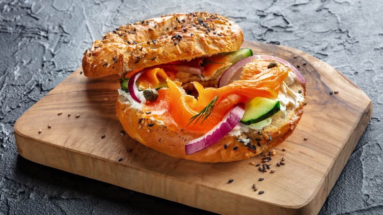A sandwich with smoked salmon and fresh vegetables on a wooden board on a black background