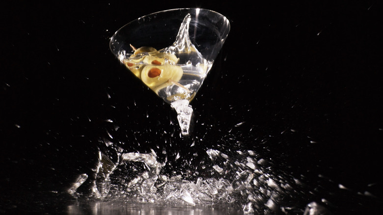 A martini with an olive appears to be in a shattering glass on a black background.
