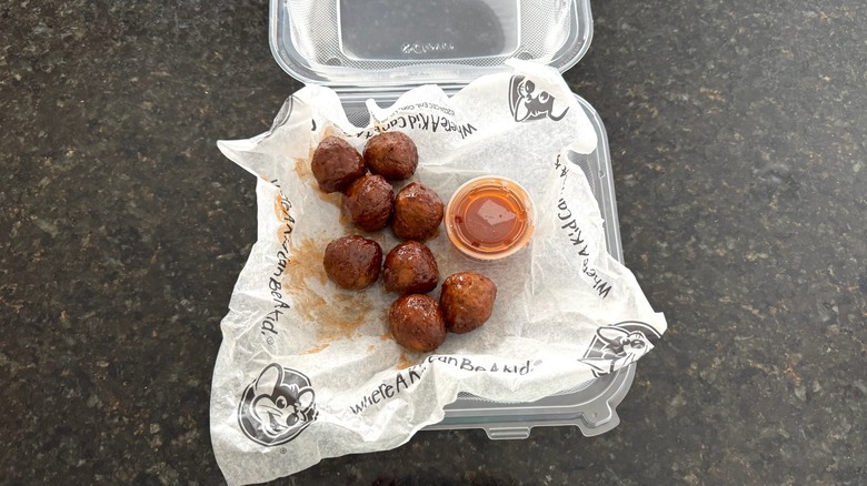 A takeout box of Chuck E. Cheese meatballs on black table