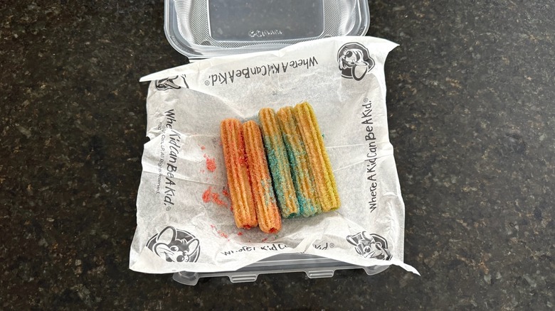 A takeout box of Chuck E. Cheese Unicorn Churros on a black table