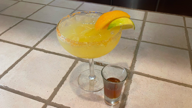 The Italian Margarita from Olive Garden on a white bar top with a lime and orange garnish and a shot of Amaretto next to it