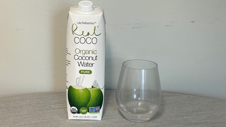 Life Refreshed Real Coco coconut water on a table beside a glass of the product